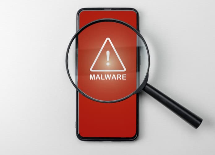 Lupa sobre celular com sinal de alerta detectando malware. Vírus sob a lente, representando aplicativo malicioso encontrado por antivírus