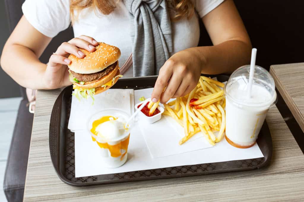 Bandeja com sanduíche, sorvete e batata frita; o lanche está na mão de uma mulher