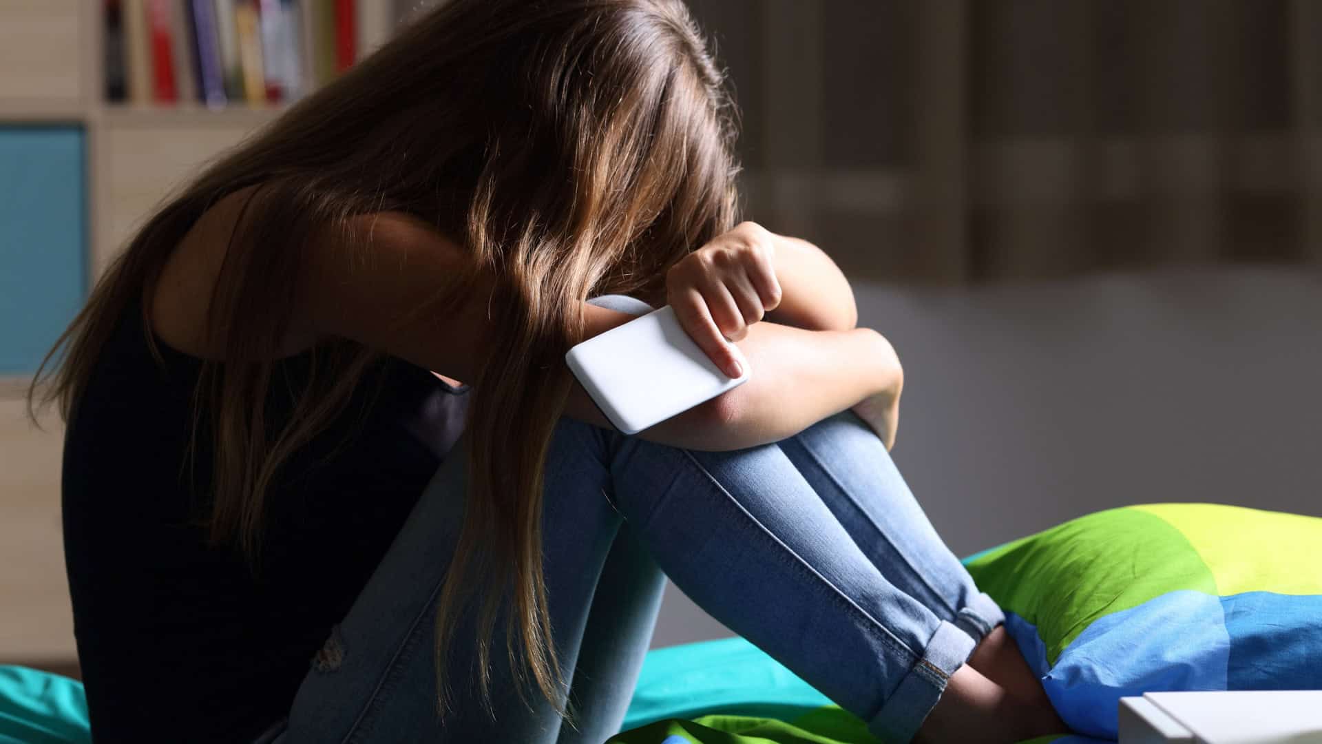 criança triste com um celular na mão