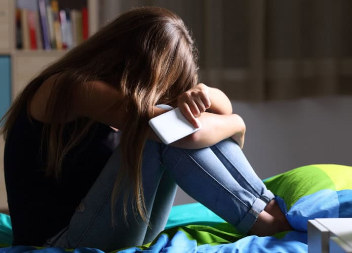 criança triste com um celular na mão