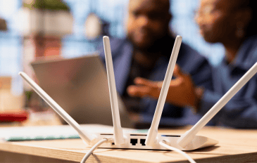 foto de um roteador em cima de uma mesa com pessoas e computadores atrás