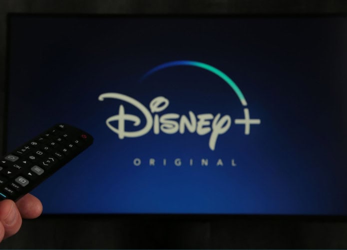 Tela de tv com o Disney+ aberto e uma pessoa com o controle remoto