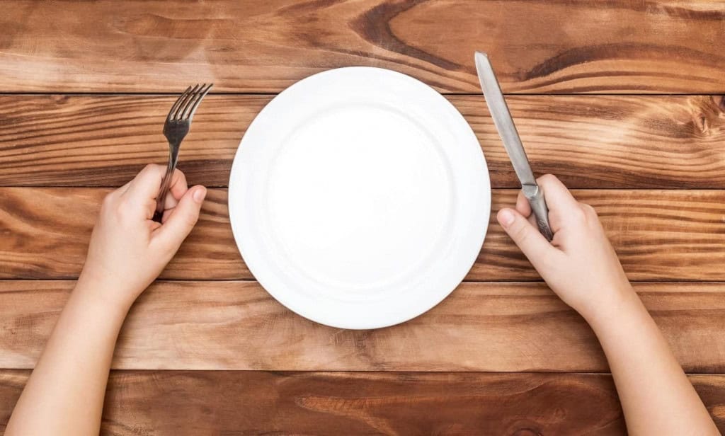 Prato de comida; em cada lado, há um garfo e uma faca em mãos de pessoa