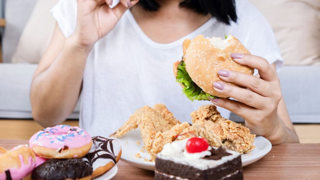 Transtorno de compulsão alimentar: mulher consumindo fast food, hambúrguer, frango frito, donuts e sobremesas