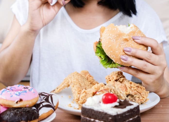 Transtorno de compulsão alimentar: mulher consumindo fast food, hambúrguer, frango frito, donuts e sobremesas