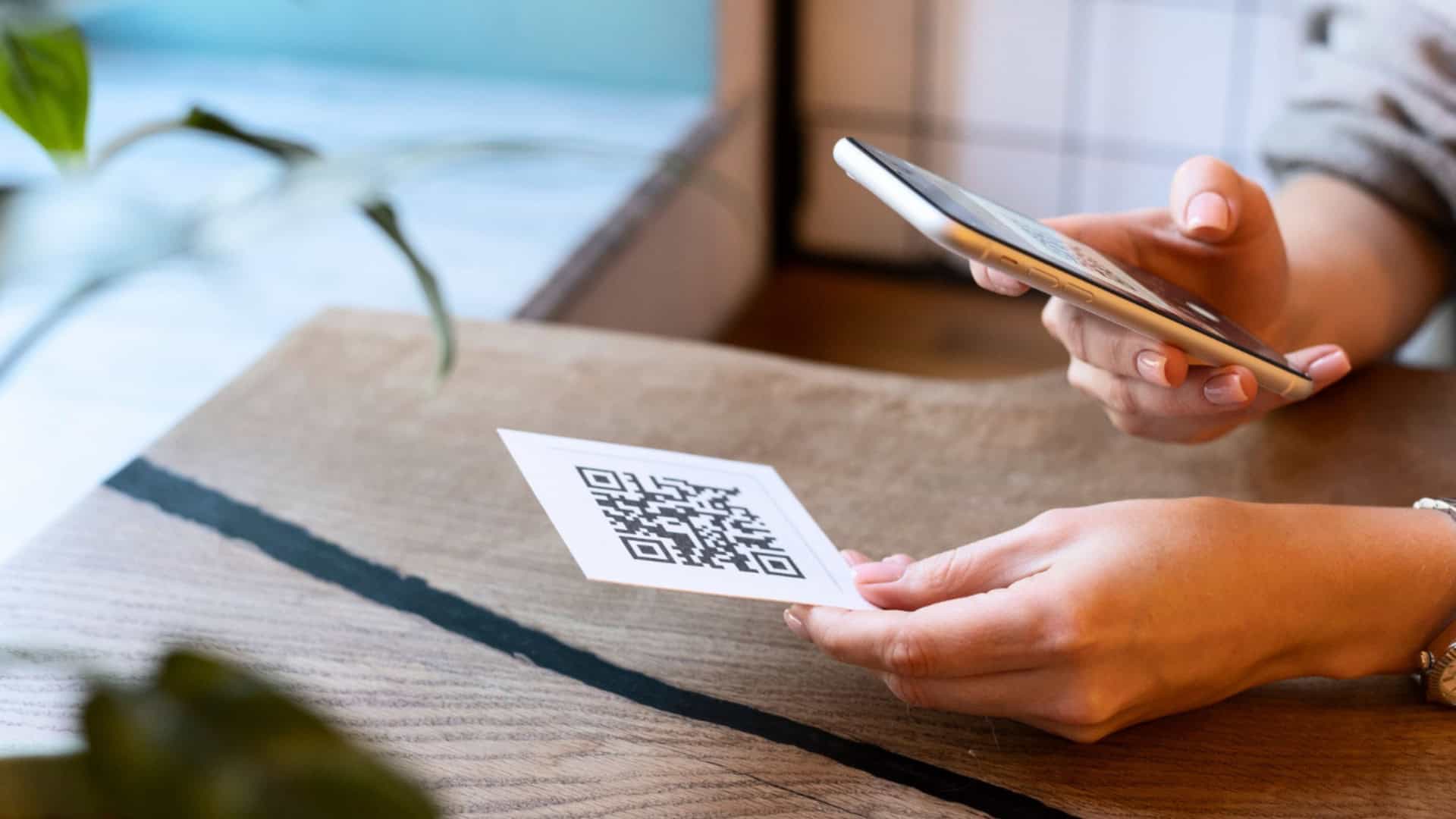 Pessoa apontando celular para um qr code em cima de uma mesa