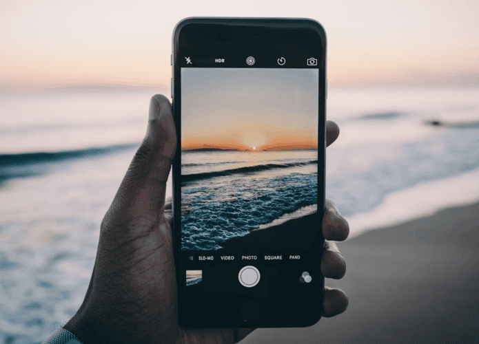 Mão segurando celular com a câmera aberta em frente ao mar