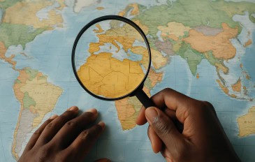 Pessoa negra segura uma lupa em cima de um mapa, ampliando o continente africano