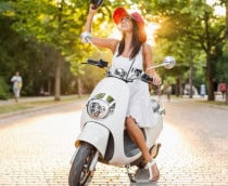 Mulher sorridente atraente andando de moto na rua com roupa estilo verão