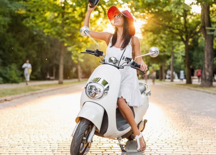 Mulher sorridente atraente andando de moto na rua com roupa estilo verão