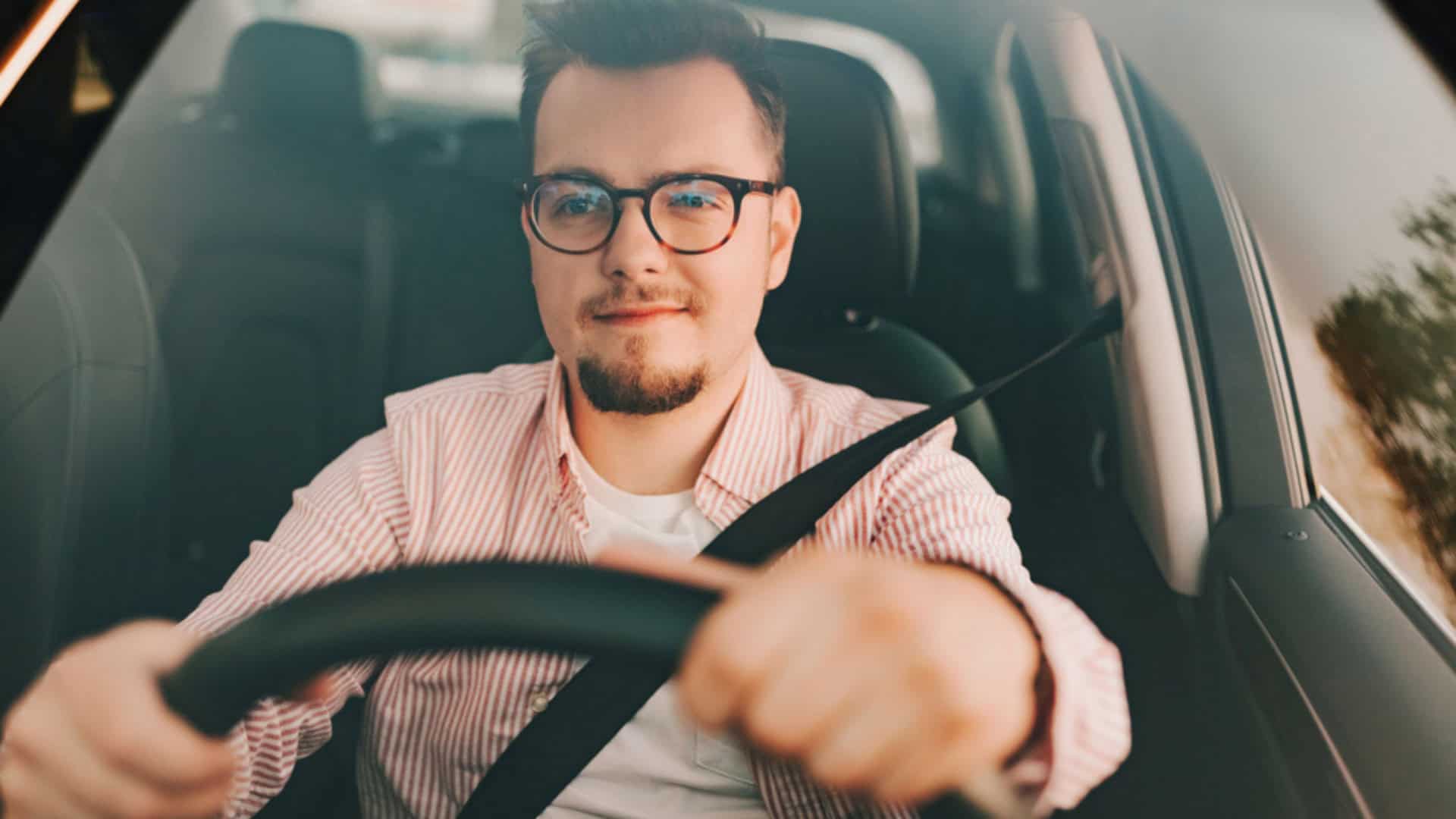imagem mostra um motorista homem com óculos de grau dirigindo um carro