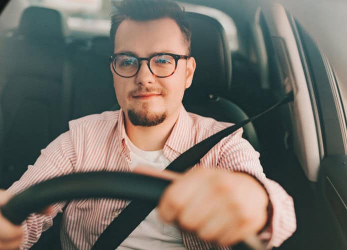 imagem mostra um motorista homem com óculos de grau dirigindo um carro