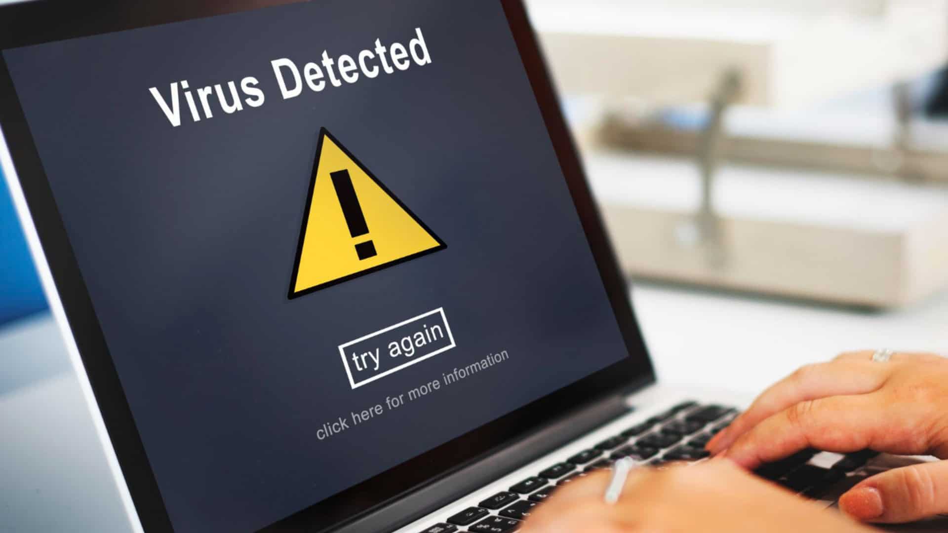 pessoa usando um laptop que tem uma mensagem de vírus na tela
