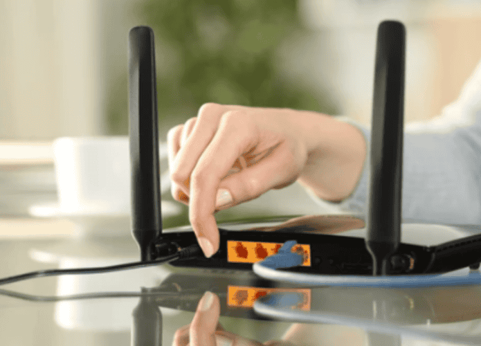 mão de uma mulher reiniciando o modem apertando o botão