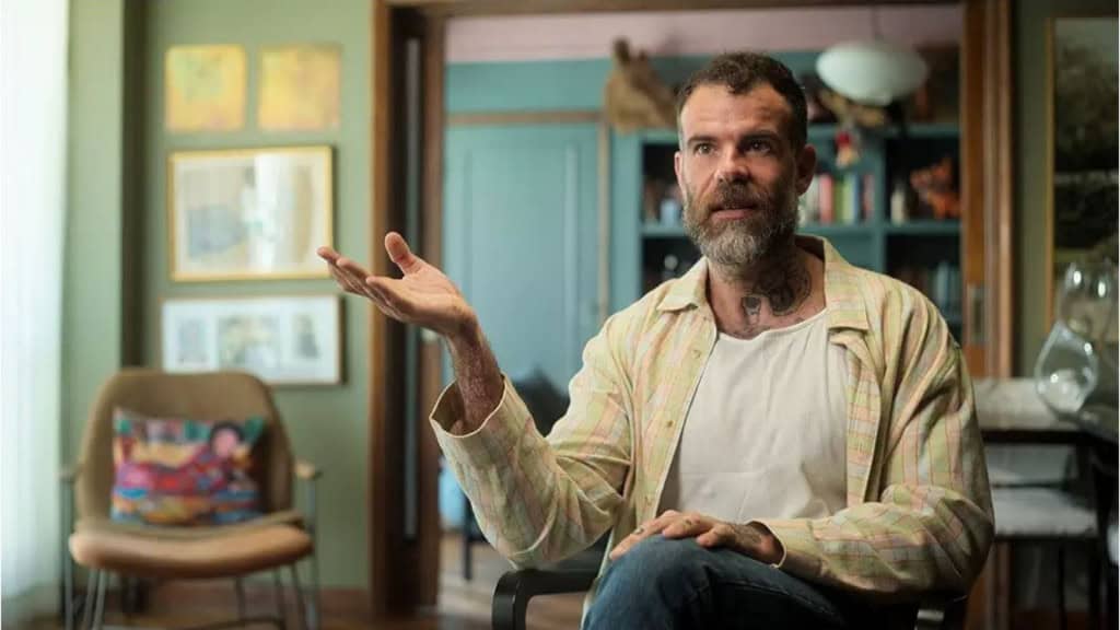 Homem sentando em uma cadeira dando depoimento para o documentário