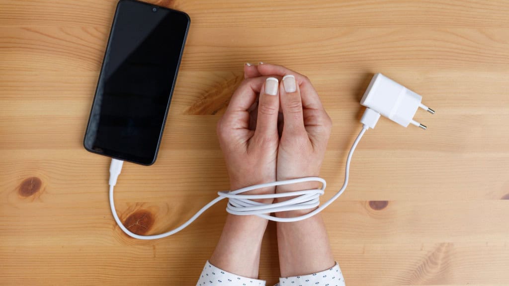 Mãos de mulher amarradas nos pulsos com cabo de celular como algemas. Vício em redes sociais