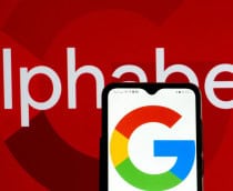 Celular com logotipo do Google na tela colocado na frente de uma tela exibindo letreiro escrito Alphabet