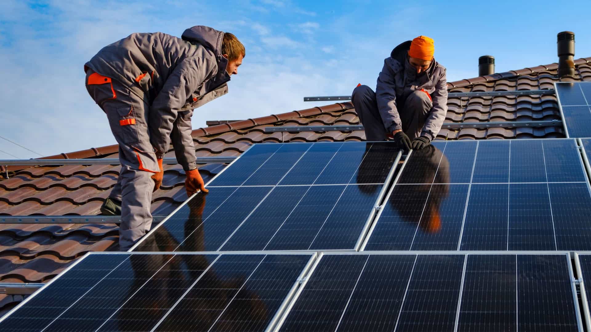 Homens instalando painéis de energia solar em telhado de casa