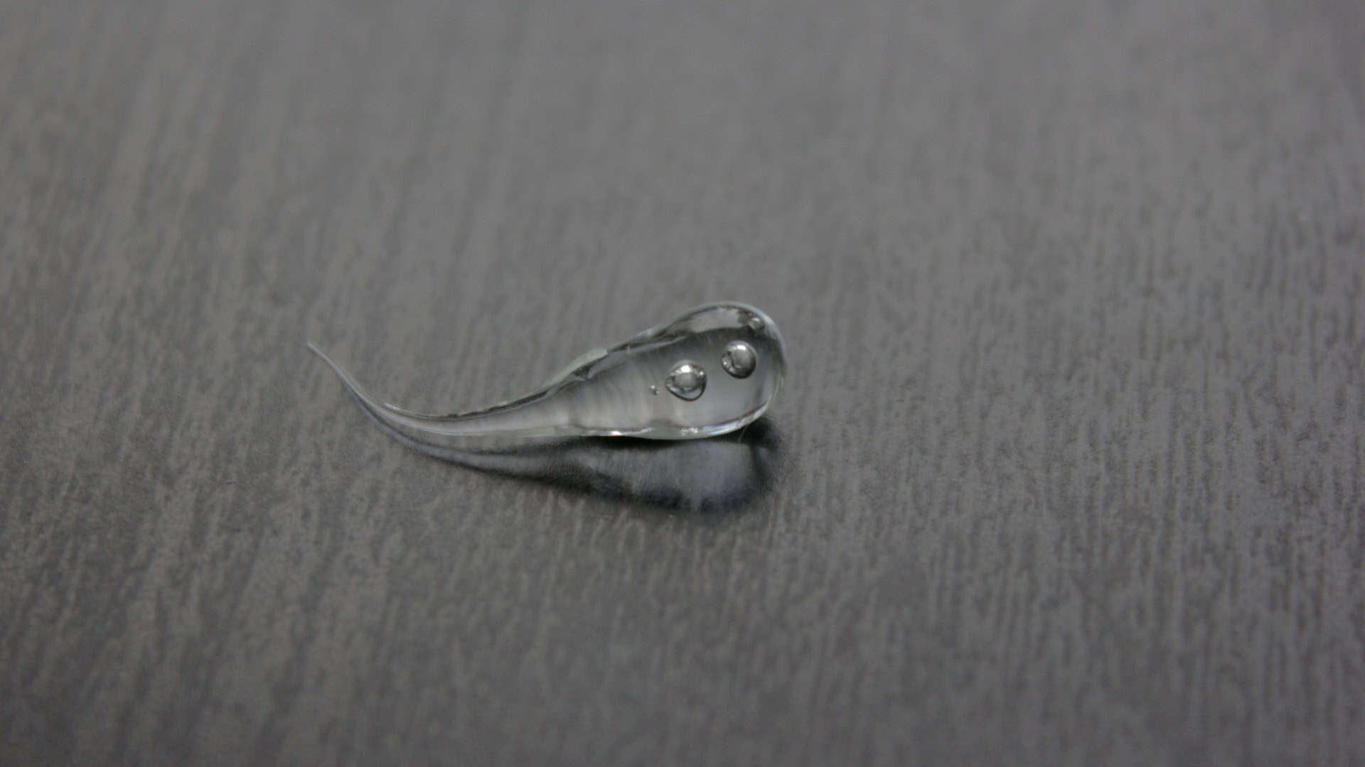 Gota de vidro, também chamada de Gota do Príncipe Rupert, em cima de mesa de madeira em imagem preto e branco