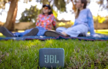 Nova caixinha JBL Go Essential 2 na grama na frente de duas moças sentadas em cima de toalha num parque