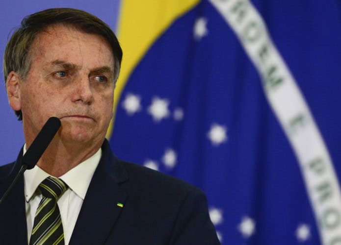 Jair Bolsonaro olhando para o lado em frente uma bandeira do Brasil