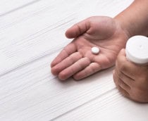 Criança com comprimido de remédio numa mão e frasco de comprimidos em outra