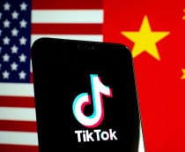 Celular com logotipo do TikTok na tela colocado na frente de uma tela com uma imagem que metade é a bandeira dos Estados Unidos e metade é da China