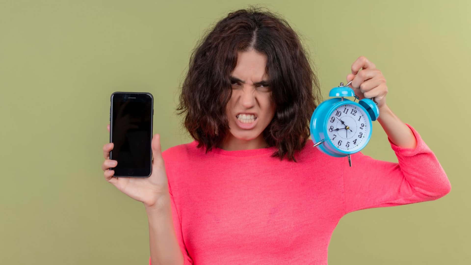 Mulher-jovem-e-bonita-com-raiva-segurando-um-celular-e-um-despertador-1920x1080