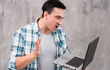 Rapaz olha o Notebook com raiva e ameça dar um tapa