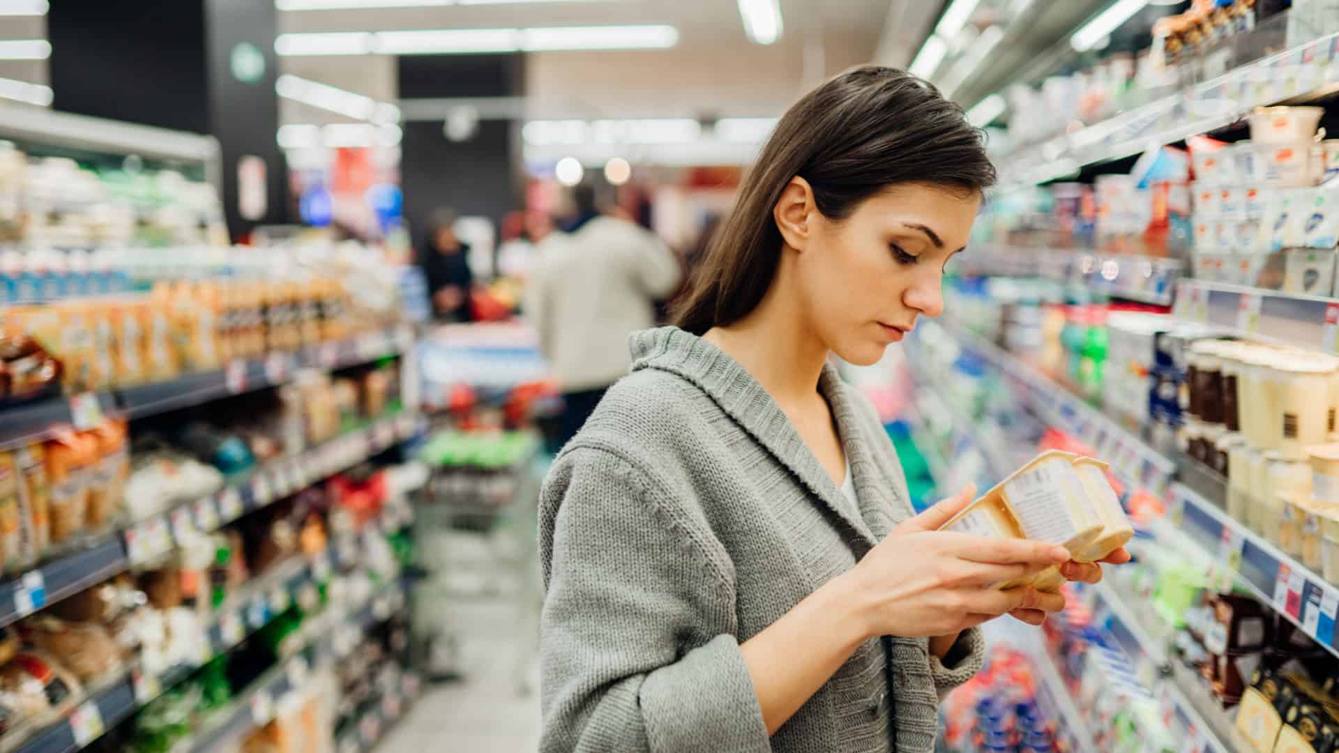Mulher lendo ingredientes e data de validade em produto lácteo no mercado
