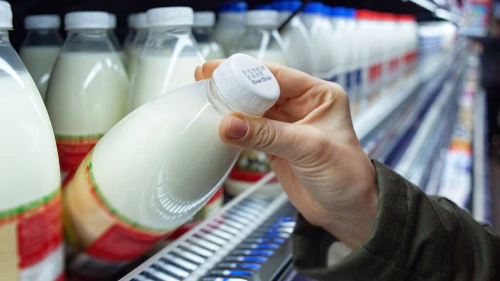 Mão segurando garrafa de leite e verificando validade no supermercado