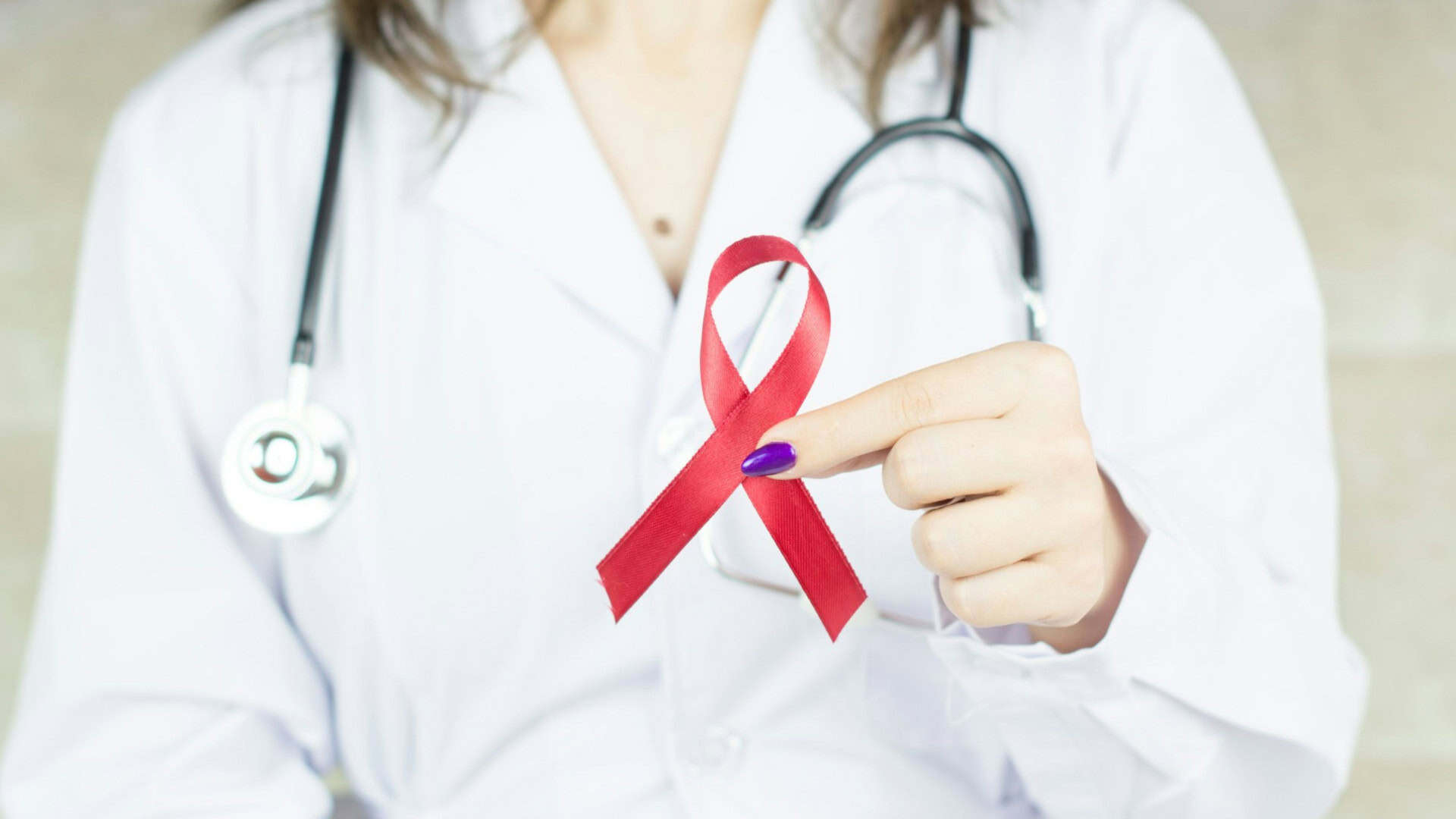 médica segurando um laço vermelho que é o simbolo da luta contra a aids