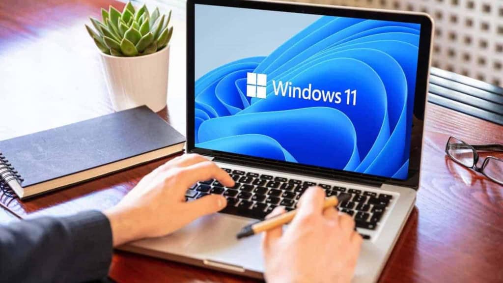 Homem utilizando um notebook com Windows 11 em uma mesa de madeira