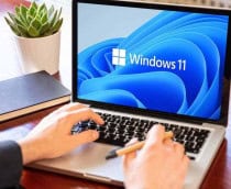 Homem utilizando um notebook com Windows 11 em uma mesa de madeira