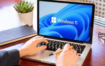 Homem utilizando um notebook com Windows 11 em uma mesa de madeira