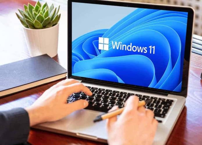 Homem utilizando um notebook com Windows 11 em uma mesa de madeira
