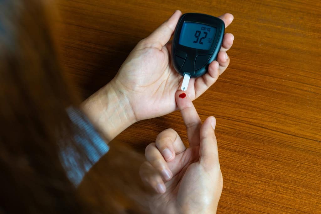 Mão de uma pessoa com um pouco de sangue, que está sendo depositado em uma tira ligada a um medidor de glicose