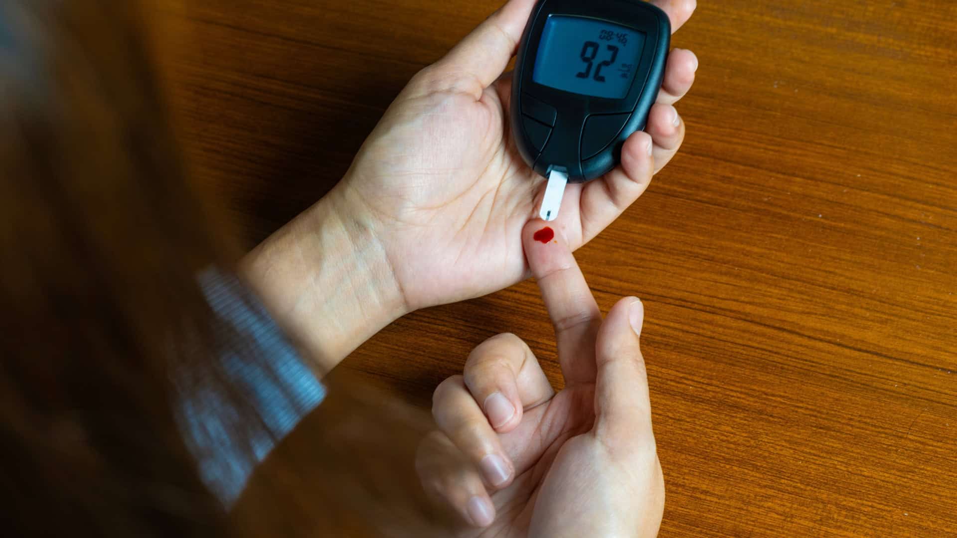 Mão de uma pessoa com um pouco de sangue, que está sendo depositado em uma tira ligada a um medidor de glicose