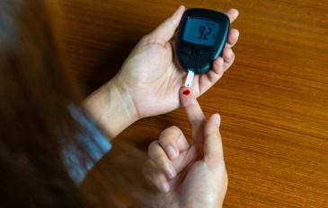 Mão de uma pessoa com um pouco de sangue, que está sendo depositado em uma tira ligada a um medidor de glicose