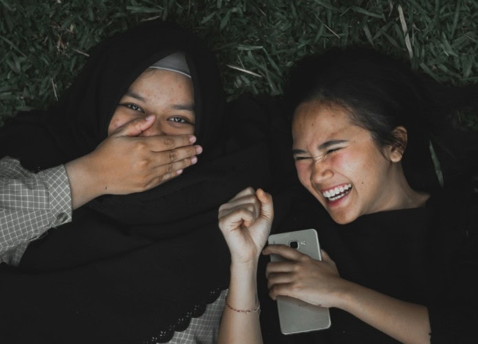 duas-garotas-meninas-deitadas-na-grama-do-cho-e-rindo-juntas-695x500