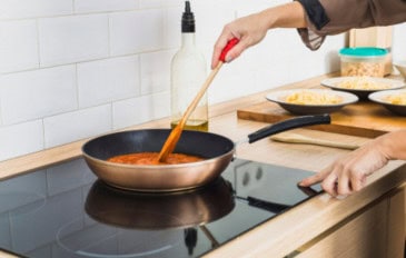 mulher cozinhando com uma frigideira em cima de um fogão de indução