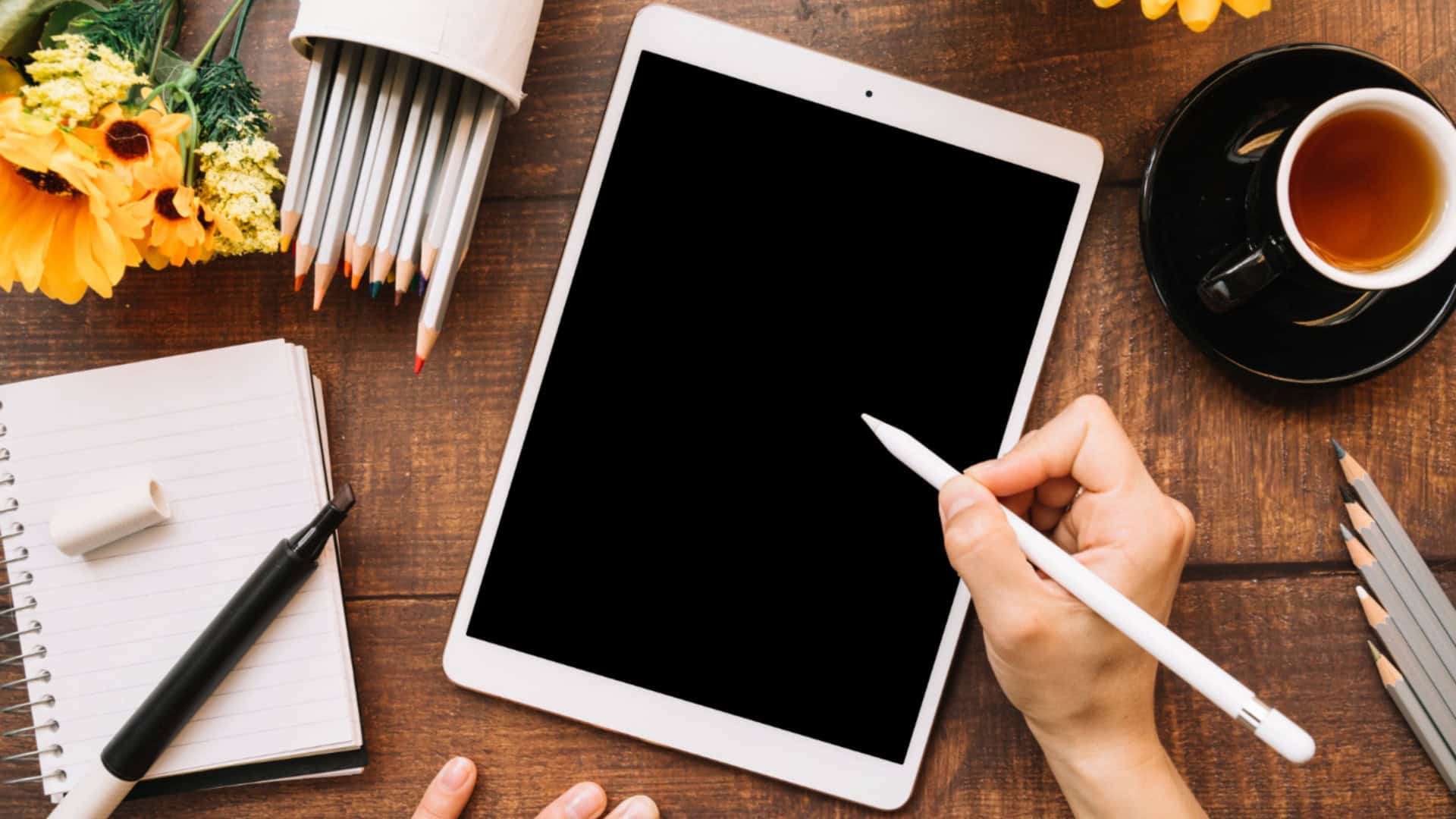 pessoa com um tablet em cima de uma mesa com objetos de escritório em volta, enquanto segura a caneta do tablet