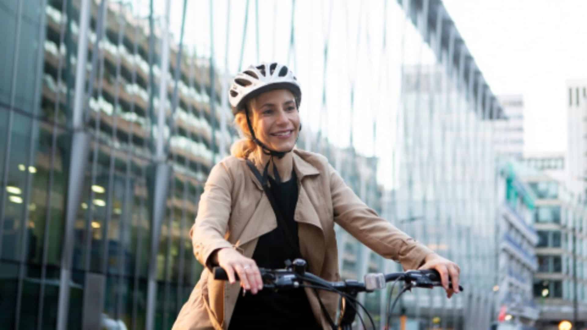 mulher de capacete com uma bicicleta no meio da cidade