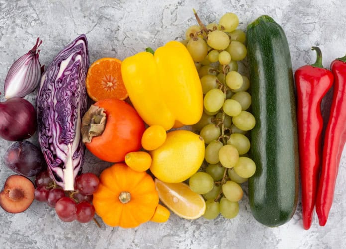 mesa com alguns vegetais, como repolho, caqui, uva, limão, pepino
