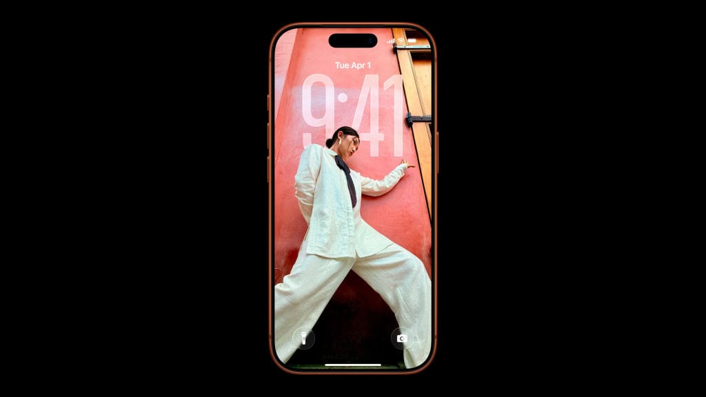 Parte da frente de um iPhone 17 Pro Max laranja mostrando tela de bloqueio com wallpaper de pessoa de lado; celular está com iOS 26 instalado
