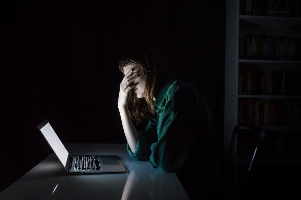 jovem no computador leva a mão ao rosto