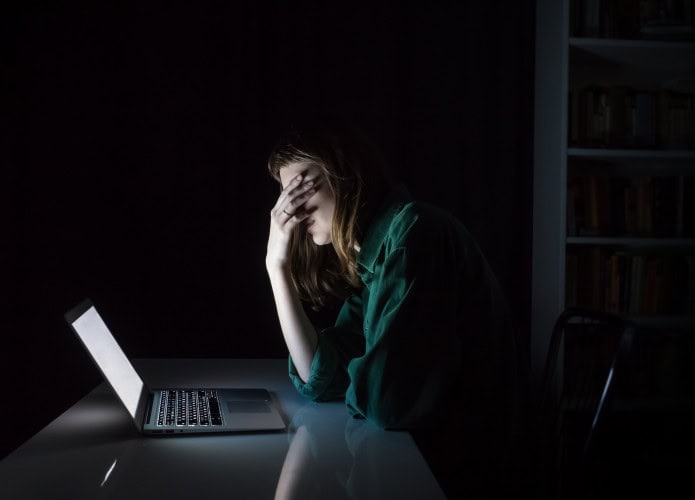 jovem no computador leva a mão ao rosto