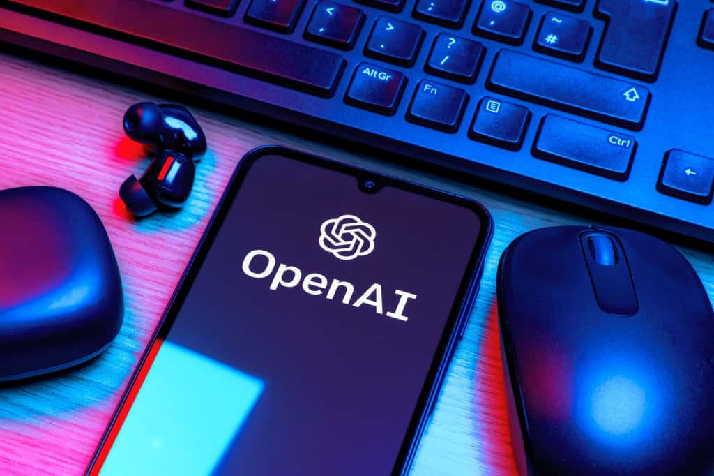 Logo da OpenAI em um smartphone que está rodeado por um fone de ouvido, um mouse e um teclado
