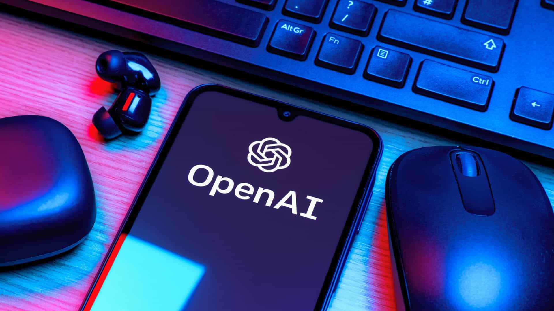 Logo da OpenAI em um smartphone que está rodeado por um fone de ouvido, um mouse e um teclado