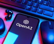 Logo da OpenAI em um smartphone que está rodeado por um fone de ouvido, um mouse e um teclado